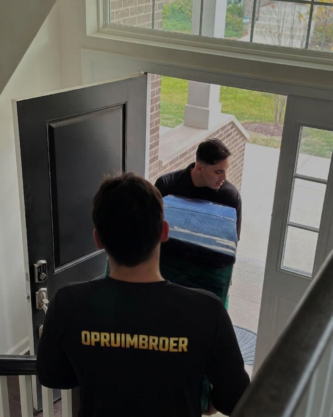 Twee medewerkers van Opruimbroer dragen een groot meubelstuk naar buiten door de voordeur
