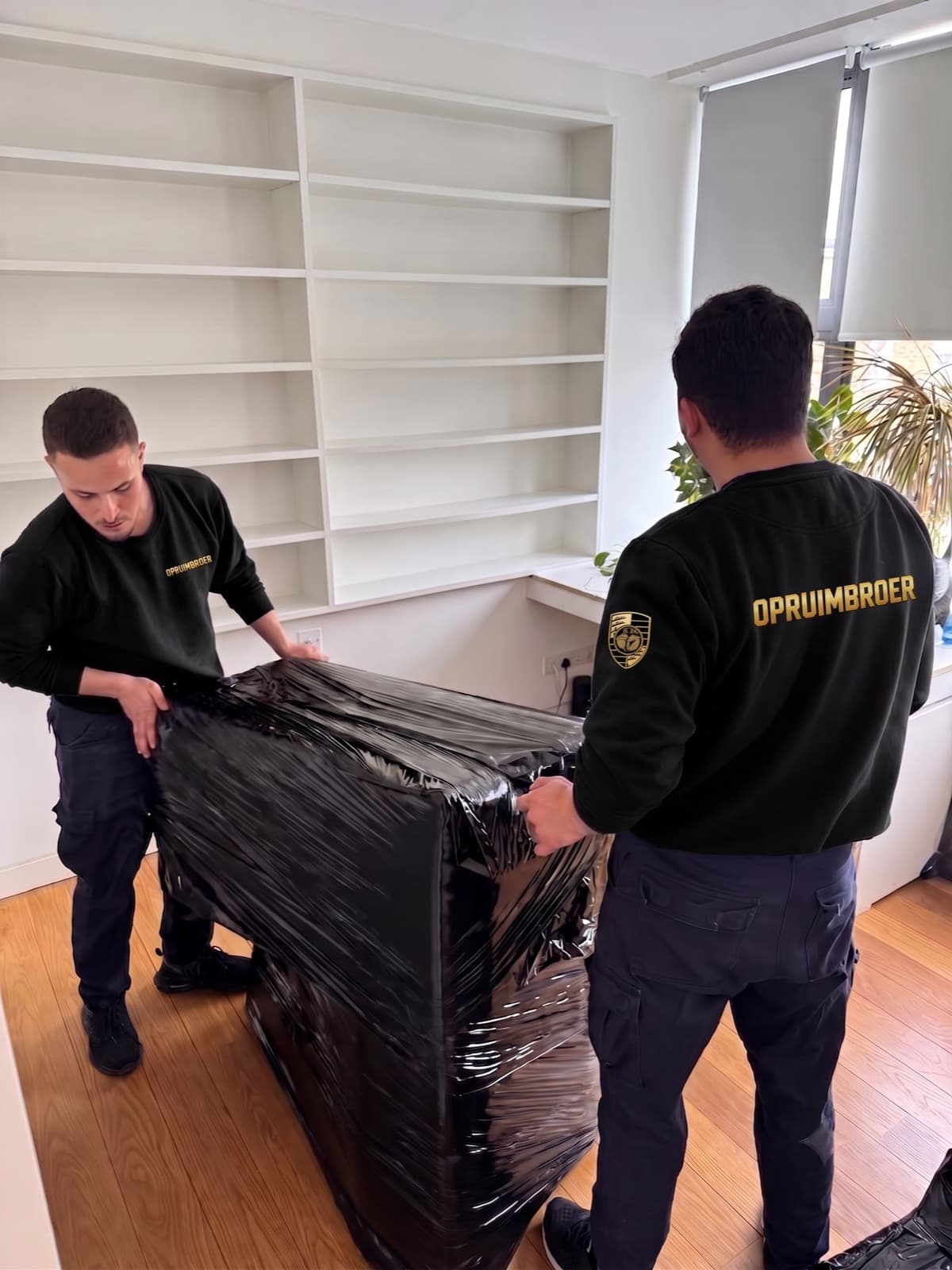 Twee medewerkers van Opruimbroer pakken een kast zorgvuldig in folie voordat ze hem afvoeren